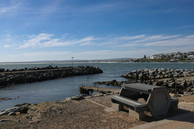 Peaceful seaside view with rocky shoreline, bench, and clear sky.